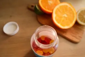 A jar of vitamin gummies beside fresh oranges — dietary supplements