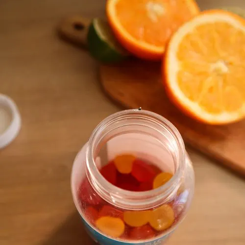 A jar of vitamin gummies beside fresh oranges — dietary supplements